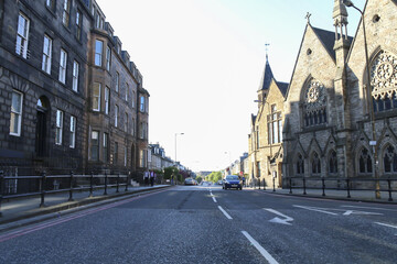 Edinburgh, United Kingdom - 15 May 2016: View of a straight road flanked by imposing stone buildings, their dark facades contrasting with the bright sky, hinting at the city's historic grandeur.