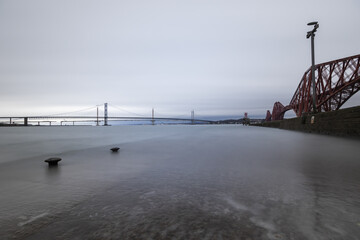 View of the Forth Bridge painted in bright red standing firm against the muted sky and the tranquil, silvery waters, Edinburgh, Scotland, United Kingdom.