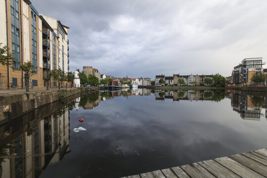 Edinburgh, United Kingdom - 23 June 2016: View of the tranquil canal mirroring the sky and modern buildings, with the subtle presence of Edinburgh Castle in the distance.