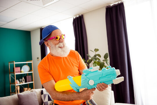 Funny grandpa enjoys indoor adventure proudly posing with neon blue toy blaster at home and weekend fun