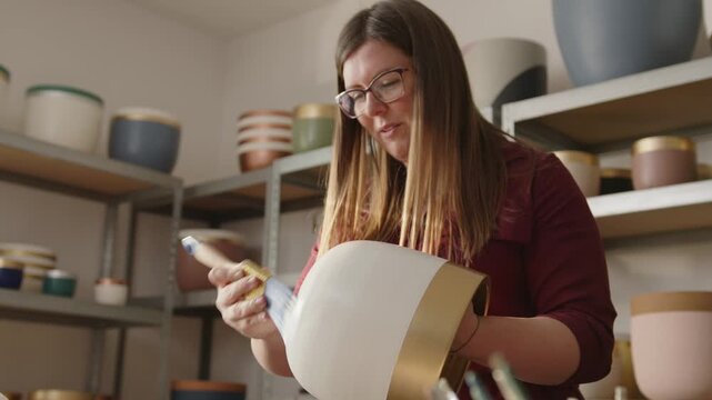 Woman painting a handmade clay pot in a ceramics workshop. Artisan applying green paint with a brush, crafting and decorating pottery in an art studio - Powered by Adobe