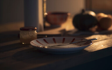 Detail of wooden table during breakfast, plate with knife, dark scene