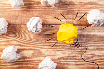 Conceptual image of crumpled paper as light bulb over wooden table