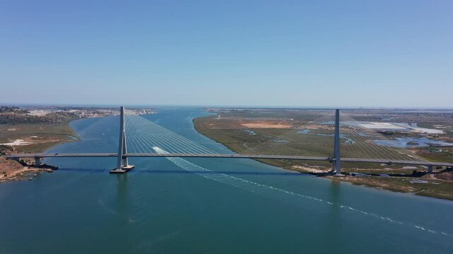 Symmetrical drone view of Guadiana International Bridge connecting Spain and Portugal over calm river with visible wetlands and boat traffic. Concept of European connectivity and modern infrastructure