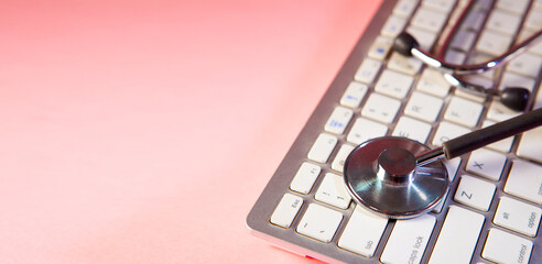 Stethoscope on a laptop keyboard on a pink background with copy space