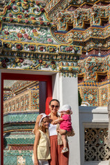 Mother and daughter standing near ornate temple structure, smiling together in sunlight, cultural heritage and family bonding travel concept