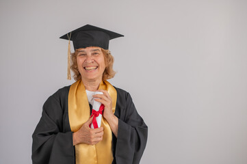 Happy senior woman in graduation gown holding diploma on white background. 