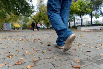 A close-up of an older man s feet walking along a leaf-covered park path, with intentional motion blur capturing movement and seasonal atmosphere.