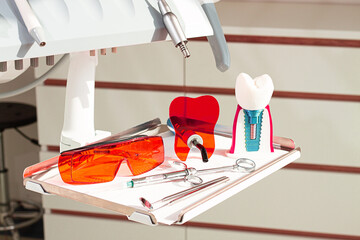 On the tray are various dental instruments, a model dental implant and bright orange safety glasses, ready for use in clinical dental settings.