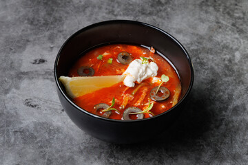 Red Tomato Soup In Black Bowl With Olive Slices, Cream
