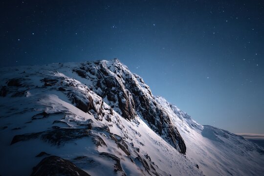 Snowy mountain peak under a starry night sky with a gradient blue background and rocky terrain visible