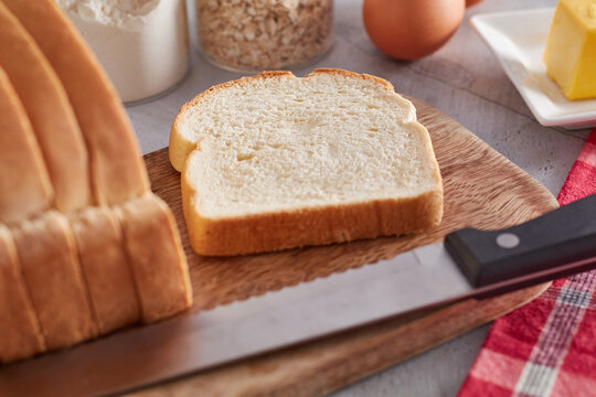 A slice of Jamaican hard dough bread on kitchen counter with eggs, butter, and oats