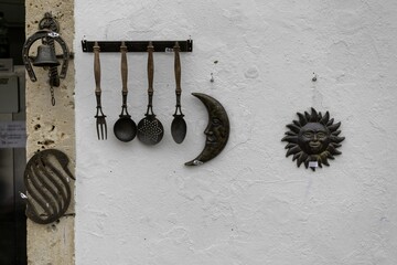 View of rustic metal craftsâ€”spoons, fork, moon, sun, bellâ€”adorning a weathered white wall, a charming display of artistry, Obidos, Leiria District, Portugal.