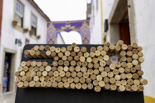 View of textured corks display a rustic charm against the backdrop of aged buildings with sunlit walls and a decorative archway, Obidos, Leiria District, Portugal.