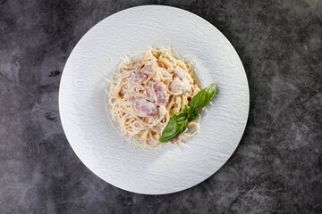 Creamy Pasta Carbonara With Bacon and Basil Garnish On White Plate