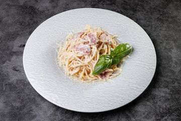 Creamy Pasta Carbonara With Bacon and Basil Garnish On White Plate