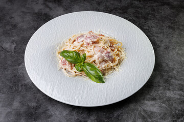 Creamy Pasta Carbonara With Bacon and Basil Garnish On White Plate