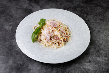 Creamy Pasta Carbonara With Bacon and Basil Garnish On White Plate