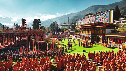 Aerial view of monks in vibrant orange robes gather in a vast courtyard, framed by ornate buildings and a backdrop of majestic mountains, Thimphu, Thimphu, Bhutan.