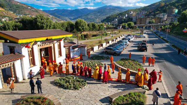 Aerial view of monks in vibrant saffron robes creating a striking contrast against the paved ground and orderly parked cars, Thimphu, Thimphu, Bhutan.