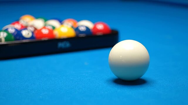 Close up of a cue ball resting on a vibrant blue felt pool table. Behind it, a set of colorful billiard balls are neatly arranged in a triangle rack, waiting for the game to begin