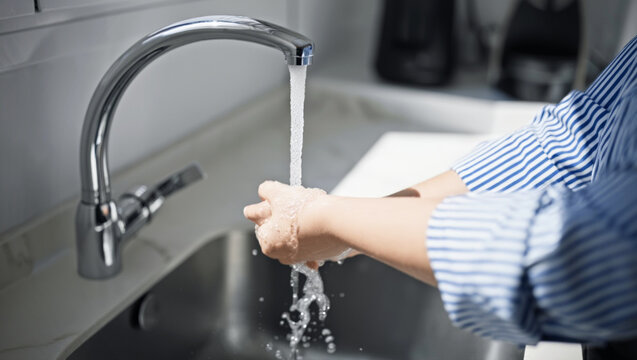 Close-up of a person's hands being washed under a stream of clean water from a modern faucet to prevent germs and maintain hygiene - Powered by Adobe
