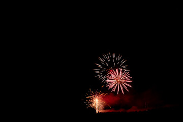 A wide photograph of red and white fireworks with a black sky and drifting smoke, with copy space.