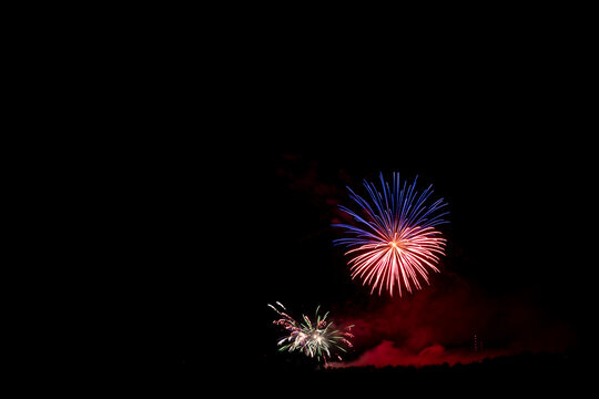 A wide photograph of red, blue and green fireworks with drifting smoke and a black sky, with copy space.