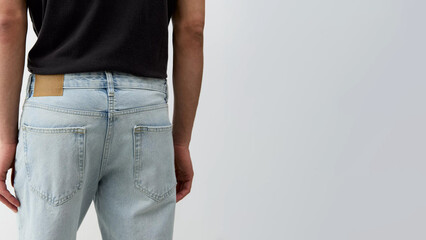 Person wearing light blue jeans and black t-shirt standing against a plain background in a casual setting.