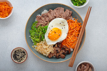 Bibimbap, authentic korean dish with a steamed rice topped with fried egg, beef, colorful vegetables, traditional dish of Korea top view on light background