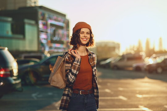 Woman shopping smile urban candid lifestyle portrait sunset with authenticity and golden hour glow; emotional storytelling of mindful living in a modern city parking lot, relaxed happy shopper with
