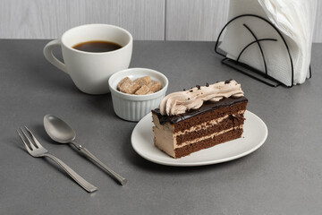 Delicious chocolate cake served with coffee, sugar cubes, and meringue on a grey table