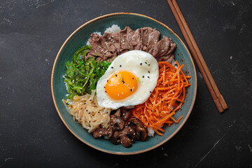 Bibimbap, authentic korean dish with a steamed rice topped with fried egg, beef, colorful...