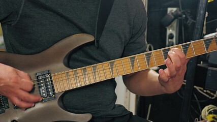 Close-up of a musician playing an electric guitar quickly. Fingers are clearly positioned on the fretboard. The setting is creative, with studio equipment in the background - Powered by Adobe