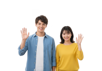 A young asian couple a man and a woman smiling and waving hello with their right hands raised against a black background