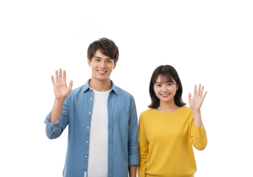 A young asian couple a man and a woman smiling and waving hello with their right hands raised against a black background