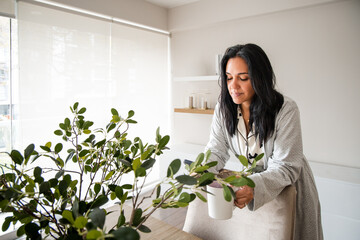 A woman is sitting in front of a potted plant and holding a cup