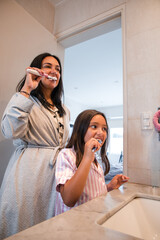 A woman and a girl are brushing their teeth in front of a mirror