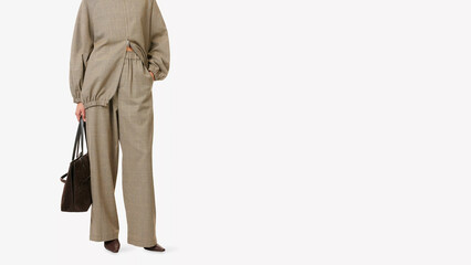 Stylish woman wearing patterned outfit poses with a bag in a modern setting during daylight hours.