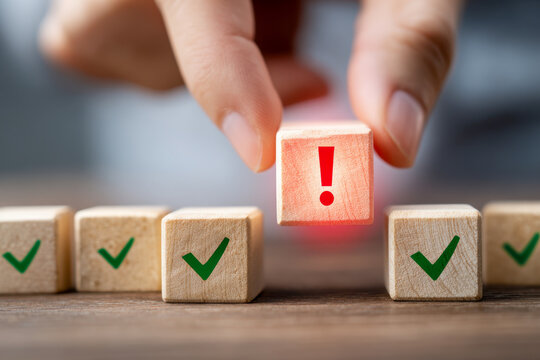 Hand placing a wooden block with an exclamation mark among other blocks with green check marks symbolizing important alerts or exceptions in a sequence of approvals