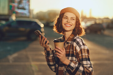 woman coffee phone smile urban golden, young woman holding takeaway coffee and phone, smiling in city light and backlight with authenticity, candid lifestyle, golden hour glow, mindful living.