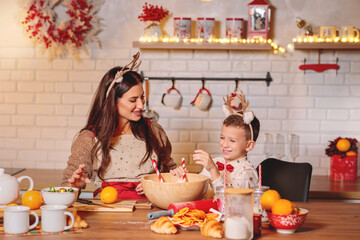 Happy mother and son in reindeer antlers baking and preparing festive treats in a warm, cheerfully decorated christmas kitchen
