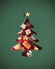 Green paper cutout Christmas tree with presents and Christmas symbols on red background. Christmas...