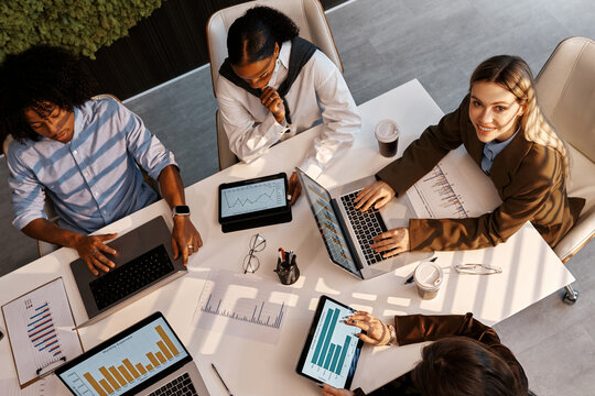 Diverse business team analyzing charts during office meeting from top view