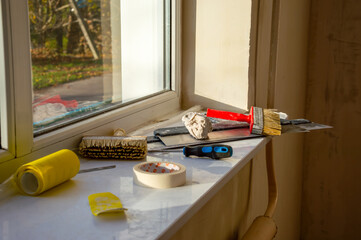 Various painting and repair tools are neatly placed on a windowsill, basking in the sunlight of a bright morning