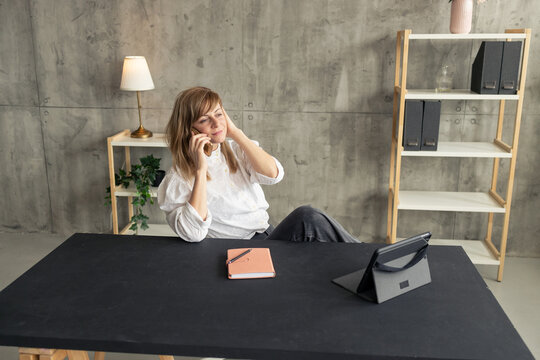 Businesswoman talking on phone in modern office: relaxed posture and productive workspace