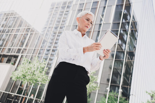 Senior businesswoman walks through a modern city outdoors with a tablet sharing ideas and plans in daylight