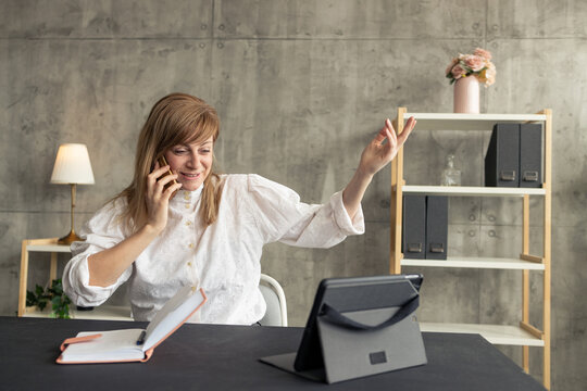 Businesswoman talking on phone and gesturing during video conference at home office