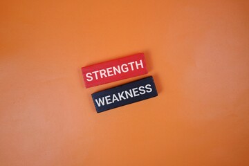 Two blocks labeled Strength and Weakness rest on an orange backdrop. Ideal for articles on self-improvement, teamwork, and decision making.
