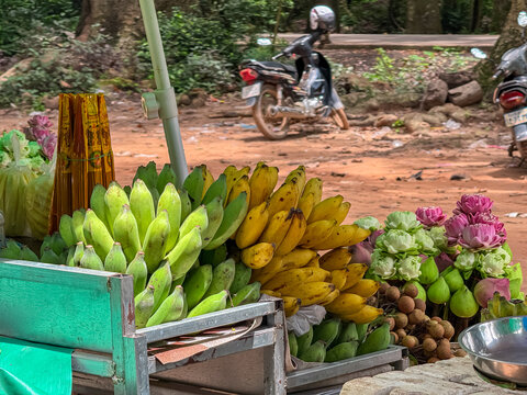 A vibrant street market stall in Siem Reap, Cambodia, displays an abundance of fresh green and yellow bananas, lotus flowers, and incense, offering a glimpse into authentic local daily life. - Powered by Adobe